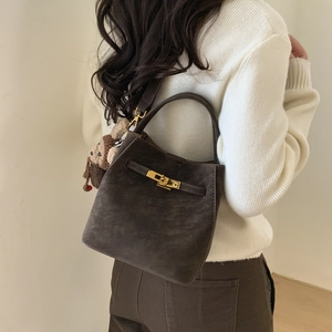 Detail of dark coffee suede bucket bag featuring golden buckle and cute monkey charm