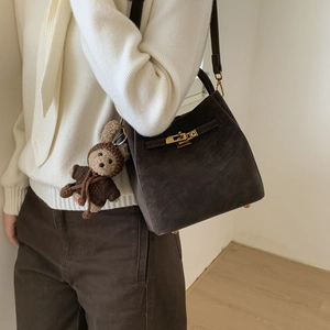 Fashionable dark coffee bucket bag with bear pendant shown in a minimal indoor setting