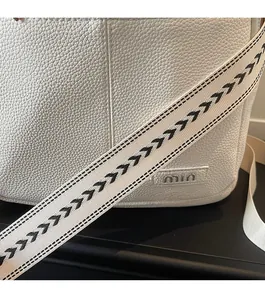 Close-up of white lychee grain leather bag with decorative black and white arrow strap