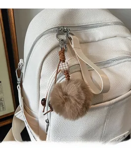 Detail of white lychee leather backpack featuring a brown plush ball pendant and silver zippers