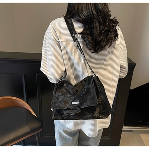 Détail d'un sac noir texturé avec boucle argentée et bandoulière chaîne sur l'épaule