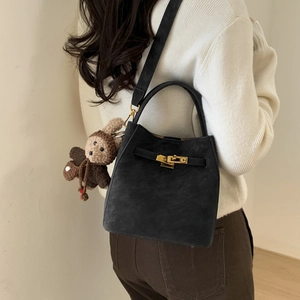 Detail of black suede trapezoid handbag with gold lock and cute bear toy pendant accessory