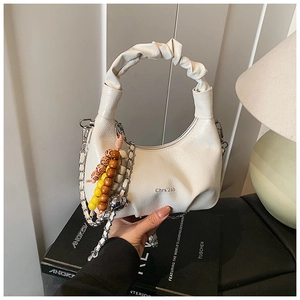 Close-up of cream-colored pleated handbag featuring a silver chain and boho beaded charm