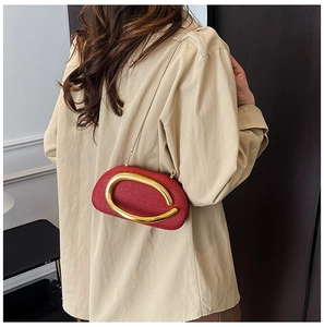 Detail of red textured acrylic crossbody bag featuring a bold gold C-shaped buckle