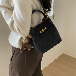 Close-up of black bucket bag with gold twist lock and cute bear charm on a model