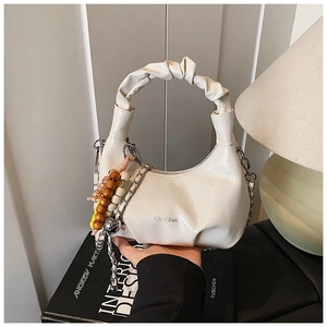 Detail of cream glossy leather handbag with ruched handle and colorful beaded charm