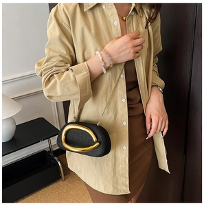 Detail of elegant black woven crossbody bag with large gold oval buckle and chain strap