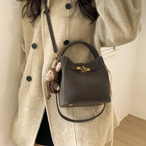 Detailed view of dark brown bucket bag with gold clasp and plush bunny charm on a model
