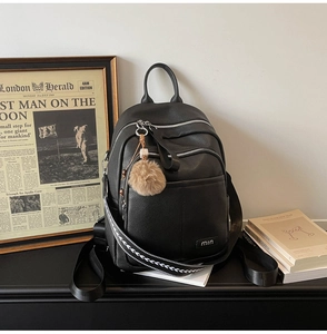 Detail of black pebbled leather backpack with woven strap and beige pompom charm