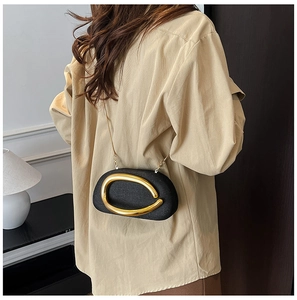 Elegant black acrylic crossbody bag with gold U-shaped buckle on a cream shirt outfit