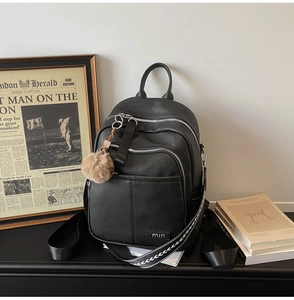 Macro detail of black litchi grain leather backpack with metallic logo and plush charm