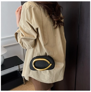 Detail of a black acrylic bag with a large gold metal buckle and a slim chain strap