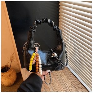 Detail of black glossy croissant bag with chain strap and beaded charm in home setting