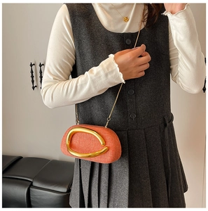 Detail of orange woven crossbody bag with large gold metal handle and chain strap