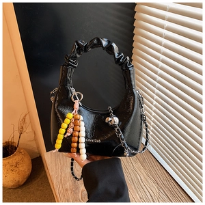 Close-up of black glossy crescent bag with ruched handle and silver chain strap