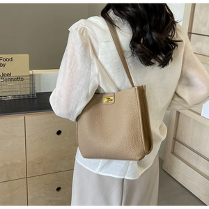 Détail du cabas en cuir grainé avec boucle dorée porté à l'épaule par un mannequin