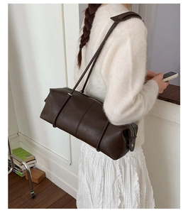 Detail view of a minimalist deep brown cylinder shoulder bag with vertical stitching