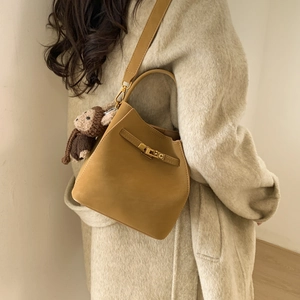 Detail of tan bucket bag with gold twist lock and cute knitted monkey charm on model