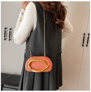 Detail of orange textured fabric crossbody bag with a large gold C-clasp and chain strap