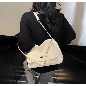 Détail d'un sac à bandoulière en cuir mat beige avec chaîne argentée sur modèle