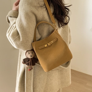Mustard yellow leather bucket bag with cute bear charm worn with a cream wool coat