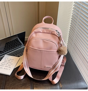 Pink pebbled leather backpack detail with patterned woven strap and brown pompom charm
