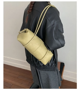 Detail view of light green cylindrical shoulder bag with sleek leather texture on model