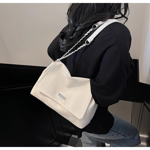 Gros plan d'un sac bandoulière en cuir beige avec chaîne argentée et plaque métal