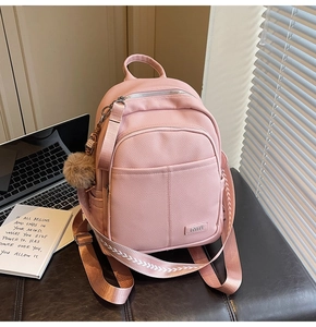 Detailed close-up of pink pebbled leather backpack with woven strap and pompom charm