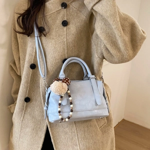 Close-up of light blue leather tote with plush charm on khaki wool coat