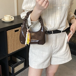 Close-up of dark brown glossy patent leather handbag with ruched handle and beaded charm