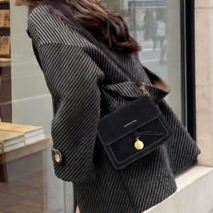 Detail of black crossbody bag with white contrast stitching and gold metal charm