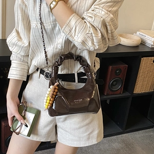Detail of dark brown patent leather dumpling bag with ruched handle and beaded charm