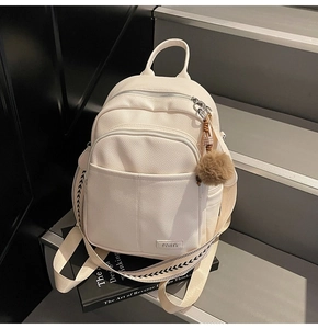 Detail view of cream lychee leather backpack with metal logo and fuzzy brown charm