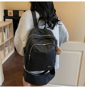 Detail view of black pebble leather backpack with dual zip front pockets and fur ball charm