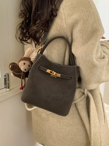 Fashionable dark gray suede bucket bag with top handle, crossbody strap, and plush charm