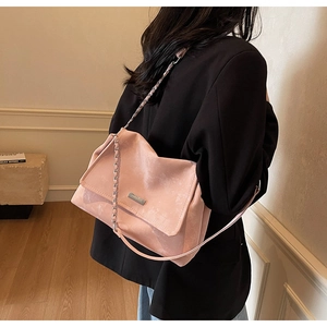 Détail du sac cabas rose texturé avec chaîne argentée porté sur un blazer noir élégant