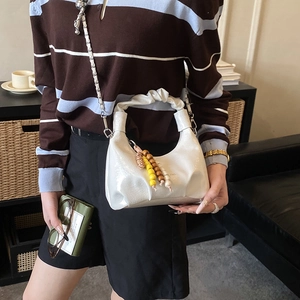 Detail of white pleated dumpling bag featuring decorative wooden beads and chain strap
