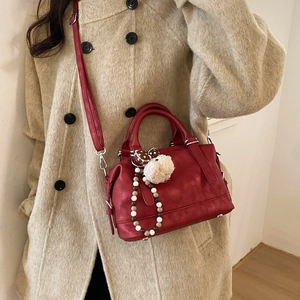Detail of red vintage tote bag with mushroom charm held by model in wool coat