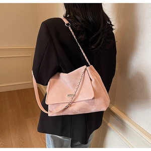 Détail du sac à bandoulière rose avec chaîne en métal porté sur un blazer noir
