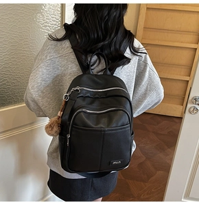Detail of black pebbled leather backpack showing multi-zipper layers and brown pompom charm
