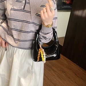 Close-up of a black patent hobo bag with glossy finish and colorful bead pendant