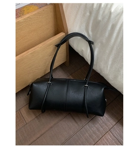 Close-up of minimalist black leather bowling bag with long shoulder strap in cozy setting