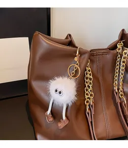 Close-up of white plush monster charm with big eyes and brown shoes on a leather bag