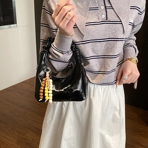 Detail of glossy black patent leather handbag with pleated handle and beaded charm accessory