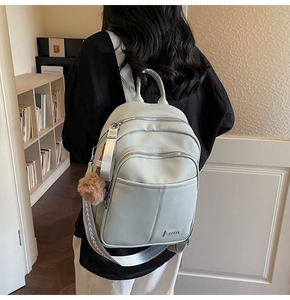 Detail of light green pebbled leather backpack with brown pompom and stylish straps