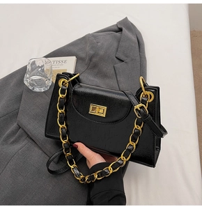 Détail d'un sac à main noir brillant avec chaîne dorée et fermoir rotatif de forme carrée