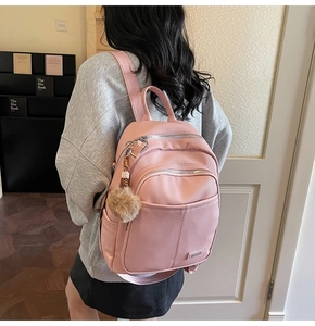 Detail of pink faux leather backpack with litchi texture and brown pom-pom charm