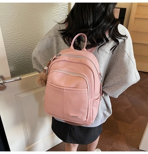Close-up of pink faux leather backpack with litchi texture and brown pompom charm