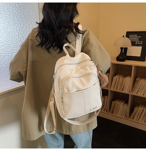 Detail of white lychee leather backpack with multiple zippers and brown plush charm